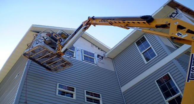 A crane is lifting up the roof of a house.